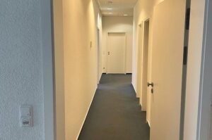 Heller, schmaler Flur mit mehreren Türen und dunklem Teppich